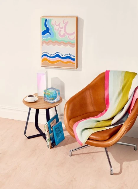 Interior featuring a brown leather chair, round table, and framed artwork with abstract coastal waves against a cream-colored wall.