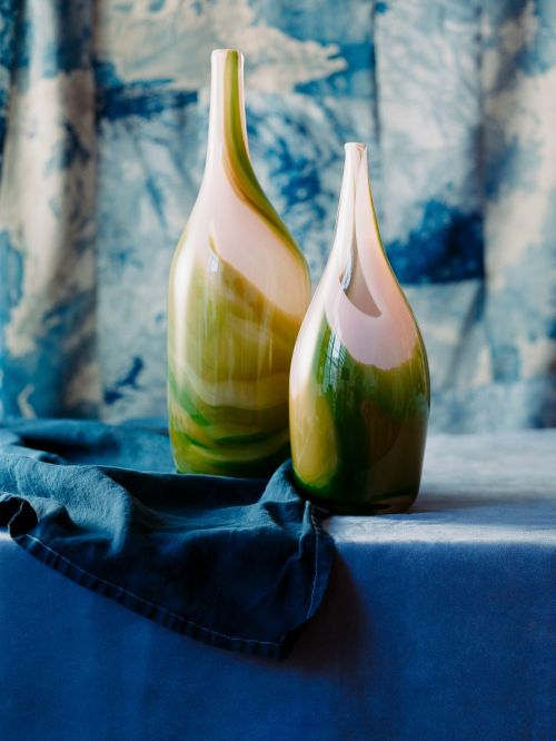 Still life of two decorative glass vases in green, white, and pink hues, positioned on a dark blue velvet surface with matching backdrop.