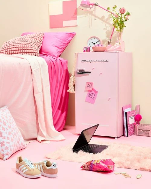 Pink themed bedroom interior with bed, mini refrigerator, laptop, and decor in a studio setting. A modern design in a monochromatic colour scheme.