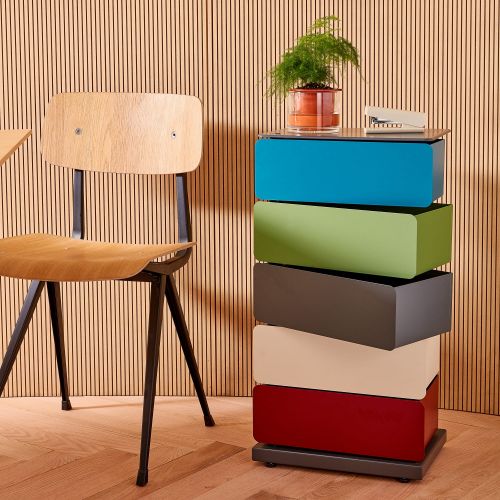 Interior view of a modern chair and colorful five-drawer cabinet, complemented by warm wood flooring and a vertically striped wall.