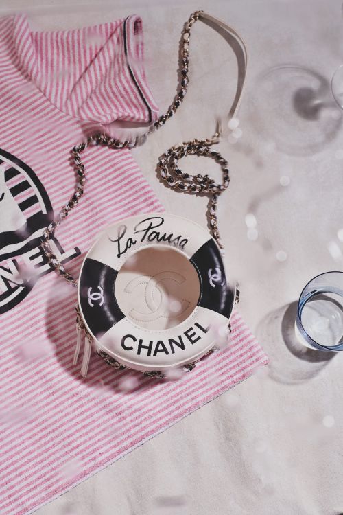 Chanel handbag shaped like a life preserver alongside a pink-striped shirt on a white surface with a glass in the background.