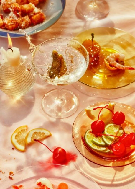 Cocktail with lime and a candle, garnished with fruit. The composition features mixed citrus, cherries, and snacks on glass plates.