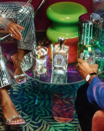 Two people at a table with cocktails, featuring a bottle of tequila, glassware, and shiny disco-inspired clothing in a lounge setting.