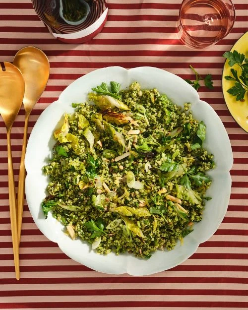 Overhead shot of a colorful, appetizing salad with leafy greens and sliced almonds served on a white scalloped plate on striped tablecloth.