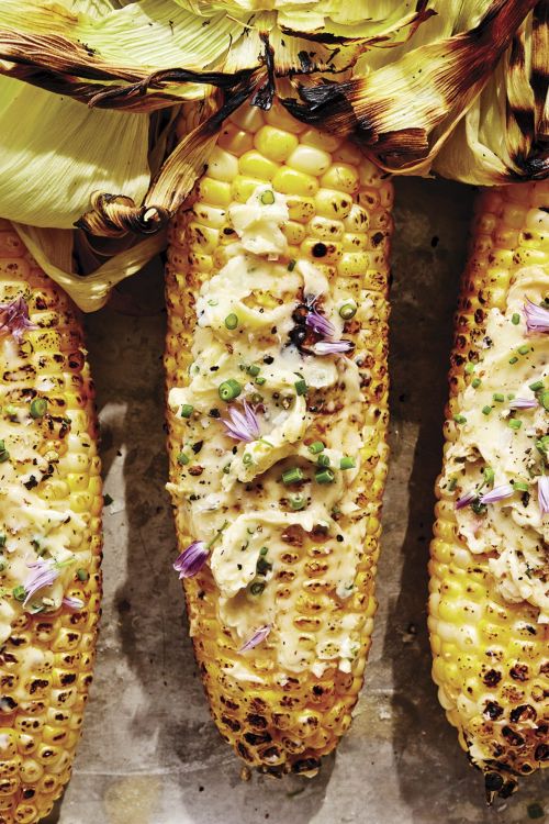 Grilled corn on the cob with herb butter and edible flowers. Close-up food photography of fresh summer food. Overhead studio shot.