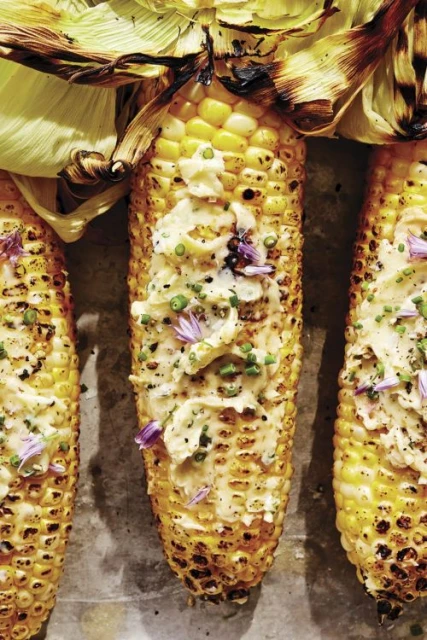 Grilled corn on the cob with herb butter and edible flowers. Close-up food photography of fresh summer food. Overhead studio shot.