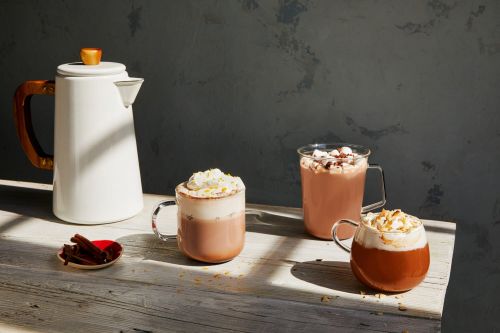Still life of hot beverages with toppings on a wooden table, against a gray backdrop, capturing cozy, inviting, and culinary appeal.