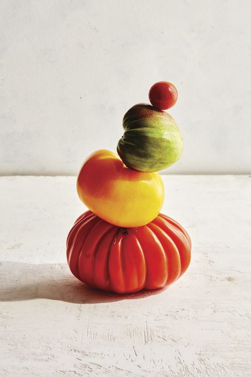 Stack of vibrant heirloom tomatoes including red, yellow, and green varieties, creating a colorful, fresh food still life.