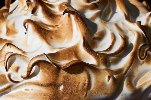 Close-up of torched meringue with browned, textured peaks and valleys, showcasing a sweet dessert with varied white-to-brown coloring.