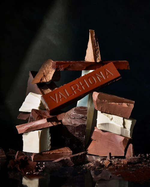 Pile of broken chocolate pieces of different types, with the VALRHONA brand name visible on one dark chocolate piece.