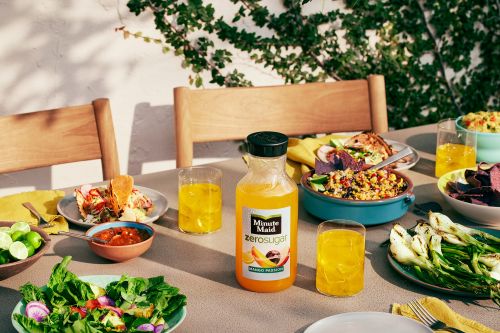Outdoor food photography of Minute Maid zero sugar mango passion juice bottle with table setting, salads, dips, and tacos.