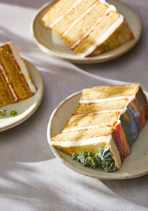 Three slices of multi-layered cake with white icing on light tan plates, presented on a light gray surface with soft shadows.
