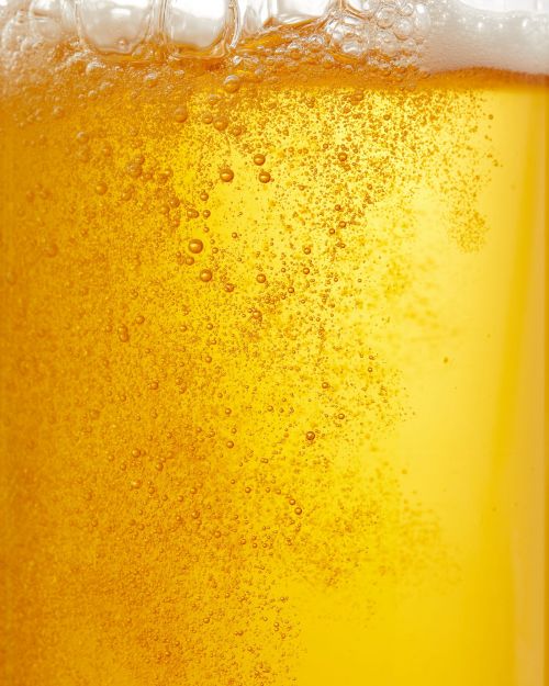 Close-up of a glass of amber-colored beer with bubbles floating throughout the liquid and a foamy head at the top.
