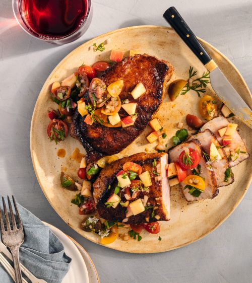 Overhead shot of a plate with grilled pork chops topped with tomato and apple salsa, accompanied by a glass of red wine.