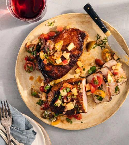 Overhead shot of a plate with grilled pork chops topped with tomato and apple salsa, accompanied by a glass of red wine.