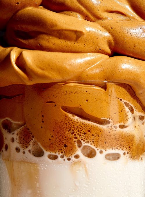 Close up macro shot of whipped dalgona coffee layered over white milk in a glass