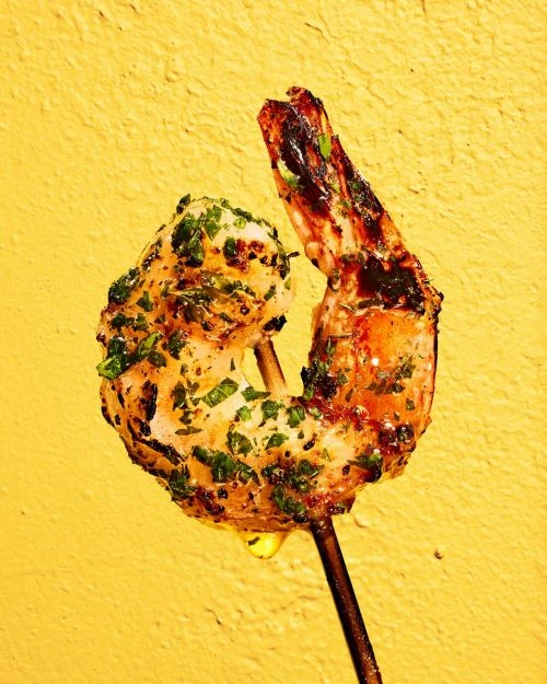 Grilled shrimp skewer seasoned with herbs on a bright yellow background with a glossy sheen, ideal for culinary content.