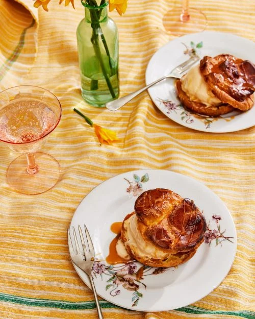Two elegant plated desserts with forks, flower vase, and champagne glass on a yellow striped tablecloth for food photography.