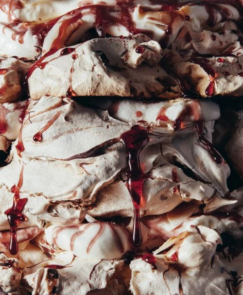 Close-up of meringue pieces stacked with red sauce drizzled on top, creating a visually striking and textured dessert composition.