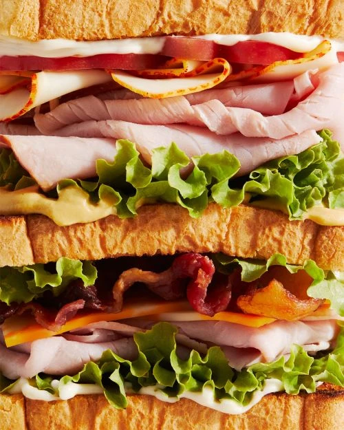 Overhead shot of a club sandwich. The sandwich is composed of toasted white bread, lettuce, tomato, bacon, cheese, ham, and turkey.