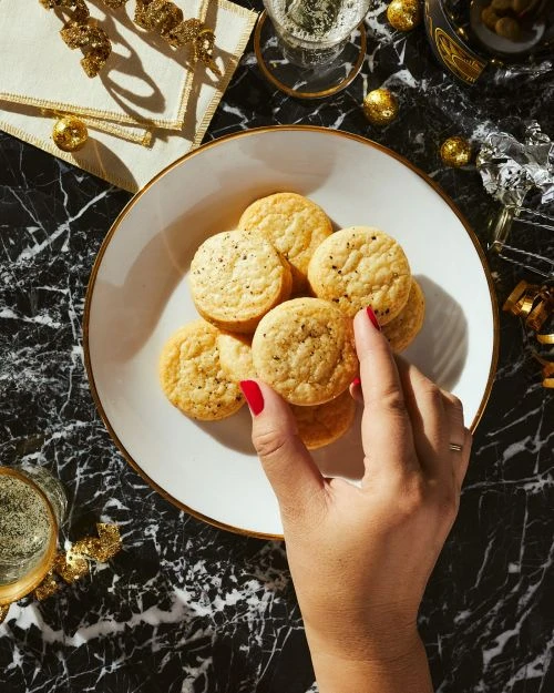 Overhead shot of a hand selecting a cracker from a plate, with champagne glasses and party decorations on a black marble surface.