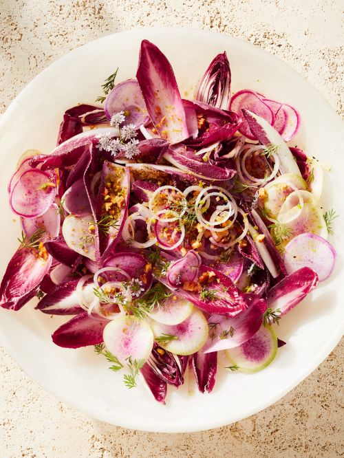 Overhead shot of a vibrant salad featuring sliced radishes, endive, and white onion rings, presented on a white plate set on a beige surface.