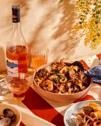 Ceramic bowl of seafood pasta, a bottle of rosé wine, and glassware on a table styled by Laura Kinsey Dolph