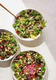 Three white bowls filled with leafy green salad, chopped vegetables, and dressing styled by Laura Kinsey Dolph.