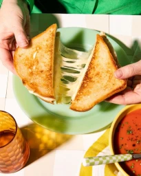 Close-up of hands pulling apart a toasted cheese sandwich with melted stringy cheese stretching between halves
