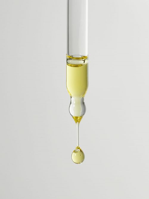 Macro close-up of a glass pipette with a drop of golden yellow liquid against a light gray backdrop, showcasing science or beauty serum.