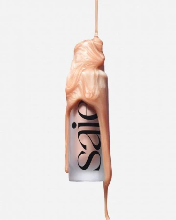 Cosmetic bottle with shiny, light-peach-colored liquid cascading down the side against a clean, bright, solid white backdrop.