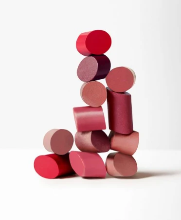 Stacked lipstick bullets in various pink and red shades against a white backdrop, suitable for makeup, beauty, and cosmetic themes.