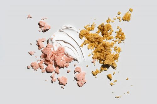 Overhead shot of pink and brown crumbles, and white cream, scattered across a light grey surface. Sweet food photography, dessert.