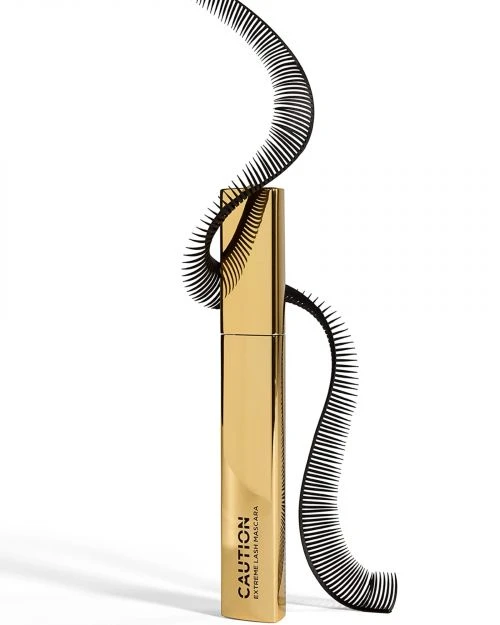 Gold tube of Caution Extreme Lash Mascara displayed with black eyelash decoration on white backdrop. Beauty product, cosmetics.