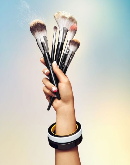 Hand holding several makeup brushes, focus on cosmetic tools with black handles, set against a gradient pastel background.