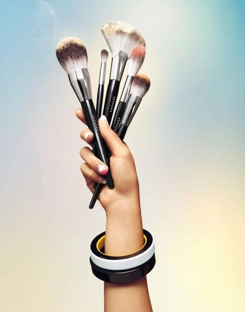 Hand holding several makeup brushes, focus on cosmetic tools with black handles, set against a gradient pastel background.