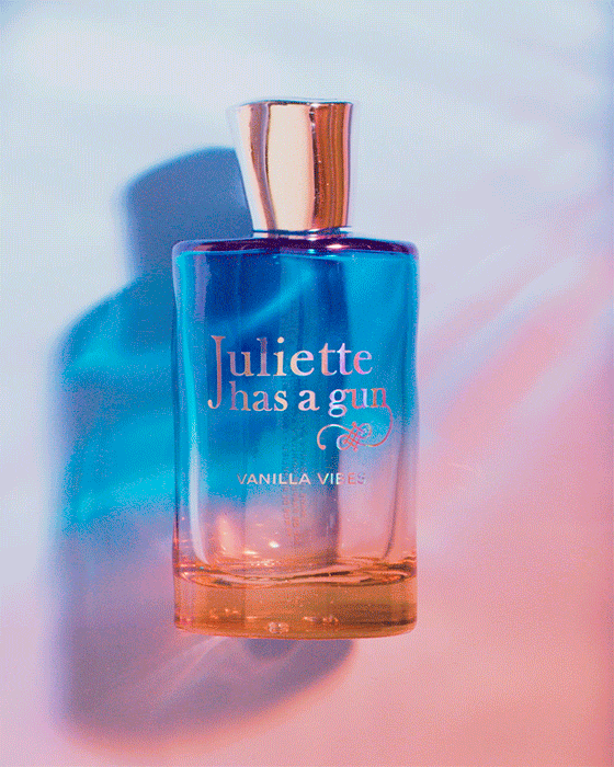 Close-up of a "Juliette has a gun" Vanilla Vibes perfume bottle in blue and orange gradient, with a golden cap and a soft, dreamy background.