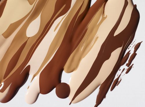 Close-up of liquid foundation swatches in various skin tones on a white background, showcasing beauty and makeup textures.