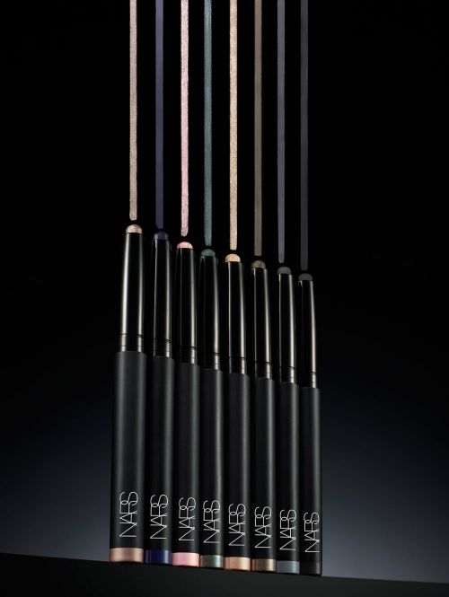Close-up studio shot of seven NARS eyeliner pencils in various colors standing upright, positioned against a dark black background.