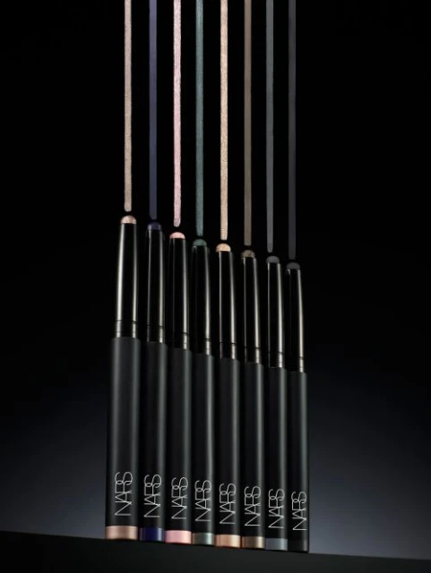 Close-up studio shot of seven NARS eyeliner pencils in various colors standing upright, positioned against a dark black background.