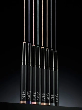 Close-up studio shot of seven NARS eyeliner pencils in various colors standing upright, positioned against a dark black background.