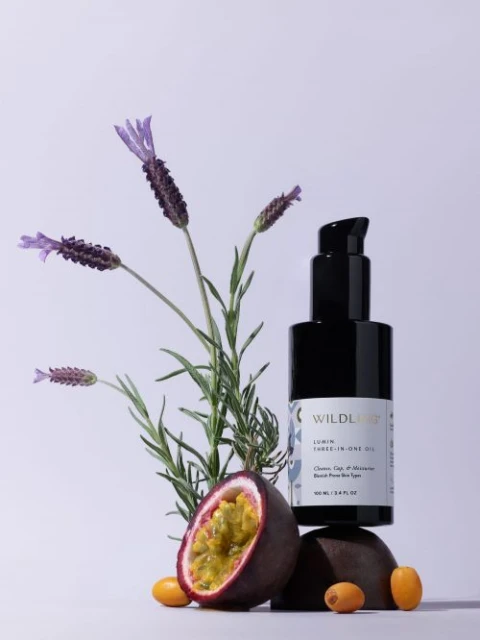 Black bottle of skincare product sits on a rock with passion fruit, kumquats, and lavender in a minimalist product shot.