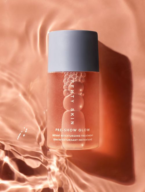 Fenty Skin 'Pre-Show Glow' instant retexturizing treatment bottle on a textured peach-colored surface with soft lighting and rippling water effect.