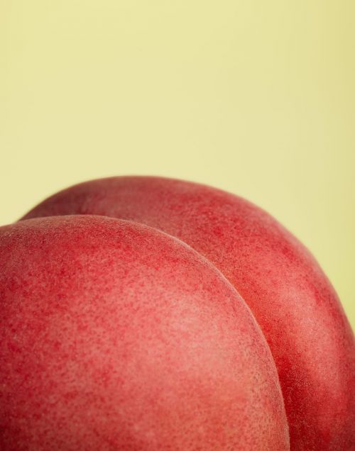 Macro shot of two ripe, red peaches against a soft yellow backdrop, highlighting their fuzzy skin texture and vibrant color.