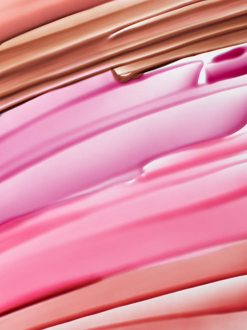 Macro shot of cosmetic product swatches in shades of pink, peach, and brown, showcasing creamy textures and makeup application.