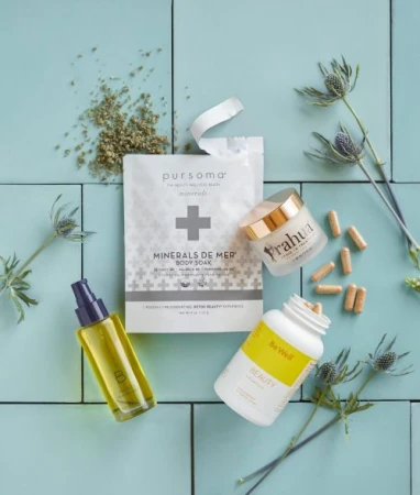Overhead shot of Pursoma Minerals de Mer Body Soak, Prahua, and Be Well Beauty supplements with scattered capsules on blue tiles.