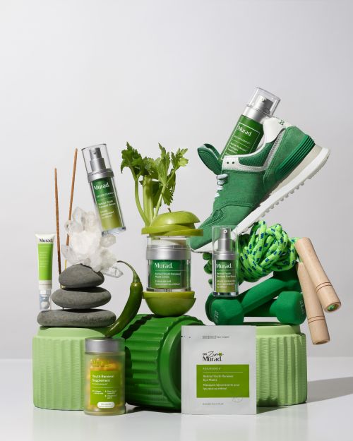Product still life featuring green Murad skincare products, arranged with fitness equipment, fruit, and produce against a white background.