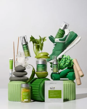Product still life featuring green Murad skincare products, arranged with fitness equipment, fruit, and produce against a white background.