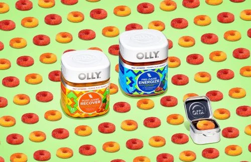 Two Olly vitamin containers, 'Post-Game Recover' and 'Pre-Game Energize,' are surrounded by ring-shaped gummy vitamins on a bright green surface.
