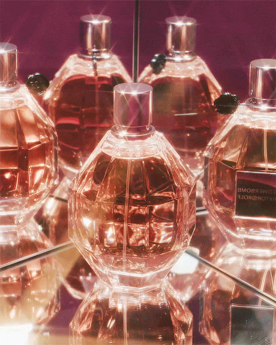 Several faceted glass perfume bottles with silver caps reflecting in a mirror against a burgundy backdrop, creating a glamorous aesthetic.